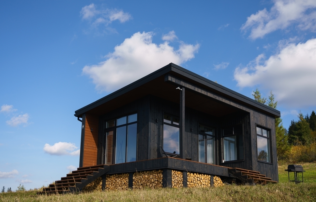 A charcoal tiny house with large glass front and a small porch with a bench.